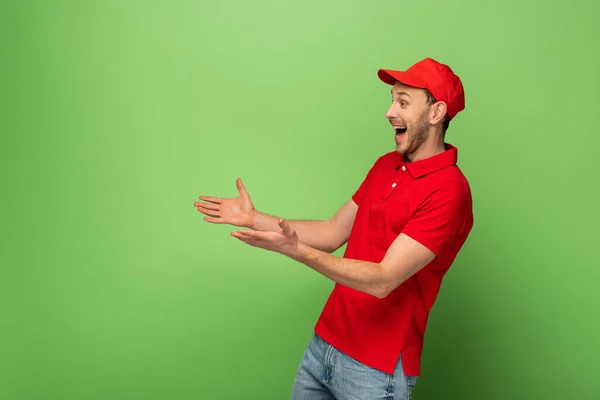 緑の背景に両手を広げて赤い制服を着た幸せな配達人の側面図 — ストック写真