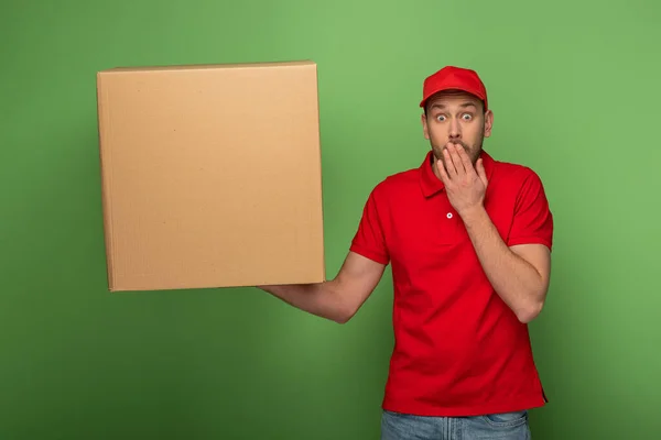 Sorprendido Repartidor Uniforme Rojo Sosteniendo Gran Paquete Cubriendo Boca Verde — Foto de Stock