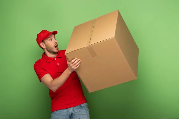 Shocked Delivery Man Red Uniform Holding Huge Parcel Green — Stock Photo, Image