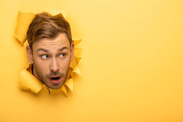 shocked handsome man with head in yellow paper hole 