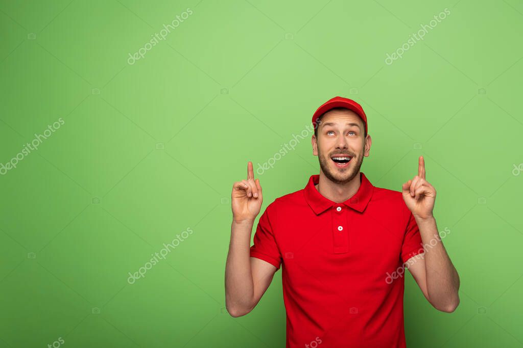 Delivery man in red uniform pointing with fingers up on green