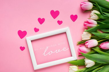 Beyaz çerçevenin en üst görüntüsü pembe arka planda lalelerin ve kalplerin yanında aşk illüstrasyonuyla ilgili her şeyi yap
