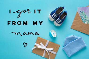 Top view of baby booties, pacifier and envelopes with greeting card on blue background, i got it from my mama lettering clipart
