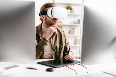 Selective focus of 3d artist using virtual reality headset and graphics tablet near computers on table clipart