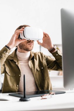 Ofisteki tablet ve bilgisayarın yanında sanal gerçeklik kulaklığı kullanan 3D sanatçının seçici odağı