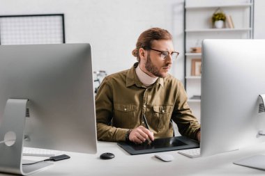 Ofisteki masadaki bilgisayarlar ve grafik tabletleriyle çalışan yakışıklı 3D tasarımcı 