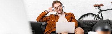 Gülümseyen 3D sanatçının seçici odak noktası müzik dinlemek ve ofisteki koltukta dizüstü bilgisayar kullanmak, panoramik çekim