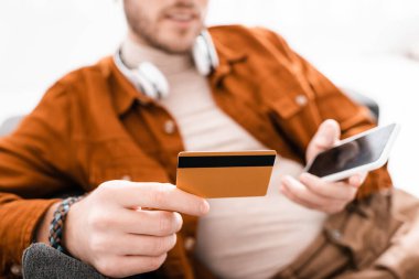 Kulaklıklı 3D sanatçının seçici odak noktası beyaz arka plandaki koltukta akıllı telefon ve kredi kartı tutuyor.
