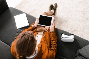 Bilgisayarın yanında boş ekranlı dijital tablet ve kanepenin üzerinde vr kulaklık tutan 3D sanatçının genel görünümü 