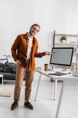 Gülümseyen 3D sanatçı kameraya bakıyor ve ofisteki bilgisayar ekranında Stylus 'u işaret ediyor. 