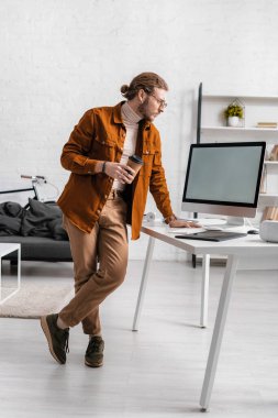Yakışıklı 3D ressam kahve tutuyor ve masadaki bilgisayar monitörüne bakıyor. 