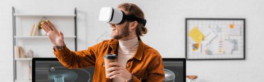 Ofisteki bilgisayar monitörlerinde 3D tasarım projesine yaklaşmak için elinde kahve olan neşeli 3D sanatçı panoramik görüntüsü.
