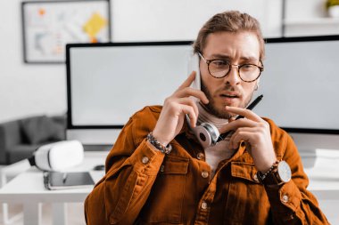 Grafik tabletinin stilini elinde tutan ve ofisteki akıllı telefondan konuşan dalgın bir üç boyutlu sanatçı.