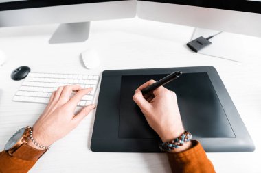 Masada grafik tableti ve bilgisayar klavyesi ile çalışan dijital tasarımcının kırpılmış görünümü 