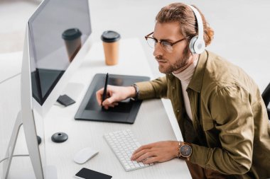Ofiste çalışırken grafik tableti ve bilgisayarları kullanarak kulaklıklarda dijital tasarımcının yan görünümü 