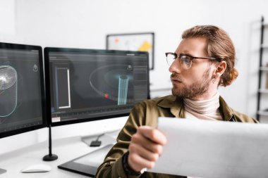 Dijital tasarımcının seçici odak noktası tablo üzerindeki bilgisayar monitörleri üzerinde 3D tasarım ve arama projesidir. 