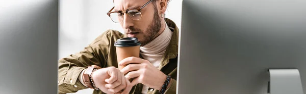白い背景にコンピュータモニターの近くのコーヒーを飲みながら腕時計を見ている3Dアーティストの選択的な焦点 パノラマショット — ストック写真