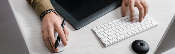 Cropped view of digital designer using computer keyboard and mouse near graphics tablet on table, panoramic shot