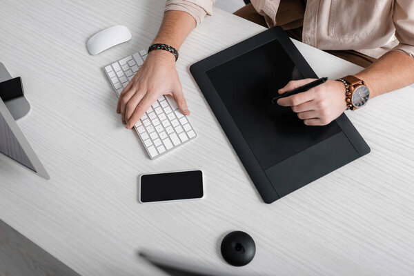 High angle view of 3d artist using graphics tablet and computer keyboard near smartphone on table 