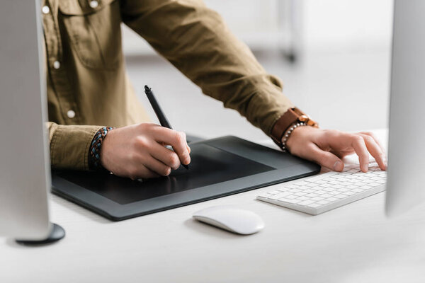 Cropped view of designer working with graphics tablet and computer keyboard on table 