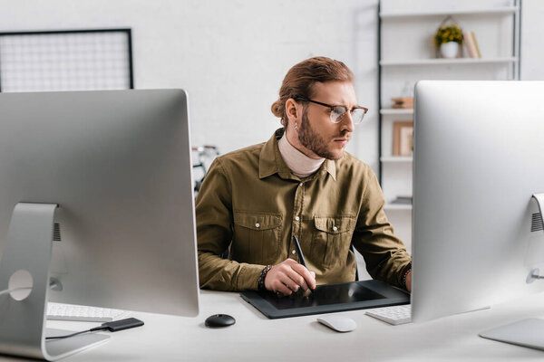 Handsome 3d designer working with computers and graphics tablet on table in office 