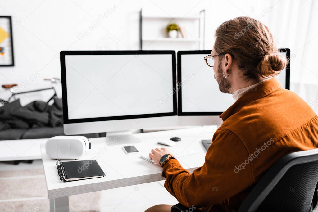 Back view of 3d artist rendering 3d project on computers at table in office