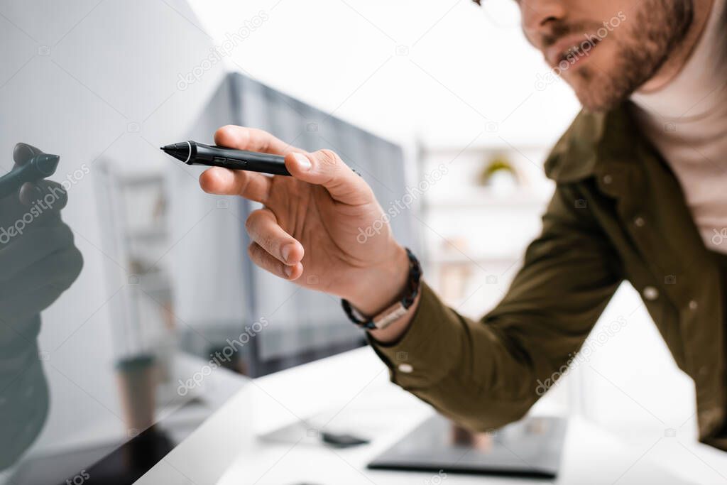 Selective focus of 3d artist holding stylus of graphics tablet near computer monitor with black screen in office