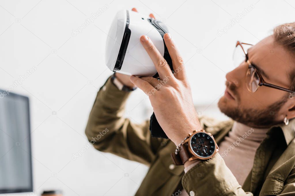 Selective focus of handsome 3d artist looking virtual reality headset in office 