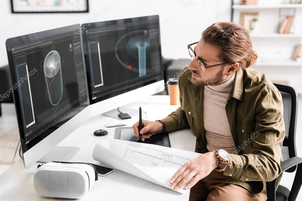 3d artist using blueprint with graphics tablet and computers while working on project of 3d design at table in office