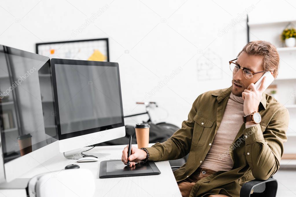 3d artist talking on smartphone and using graphics tablet and computers at table in office 