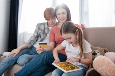 Çocuk, e-sağlık uygulamalı dijital tablet kullanıyor. Yanında da kredi kartıyla gülümseyen aynı seks ebeveyni var.