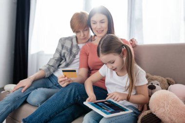 Evde kredi kartı olan annelerin yanında uygulamalı dijital tablet kullanan bir çocuk.