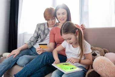 Çocuk dijital tablet kullanıyor. Evde kredi kartı olan annelerin yanında ekranda en iyi alışveriş uygulaması var.