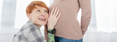 Panoramic shot of smiling woman touching tummy of pregnant girlfriend at home  clipart