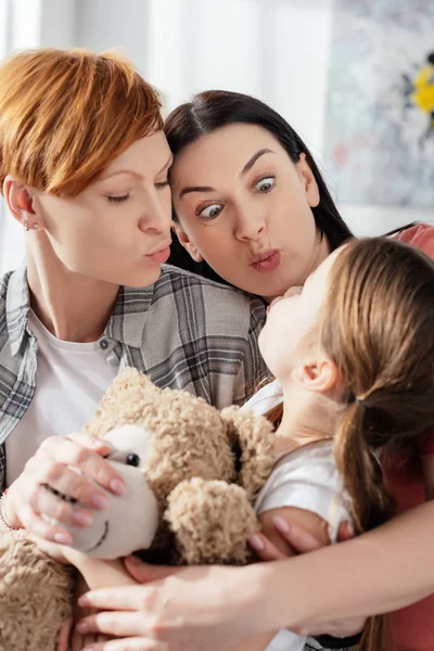 Same Sex Parents Grimacing Daughter Holding Teddy Bear Home — Stock Photo, Image