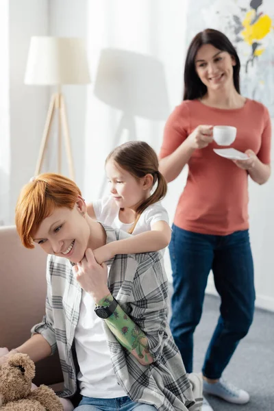 母亲与女儿在沙发上玩耍的选择性焦点 父母身边有咖啡杯在客厅里 — 图库照片