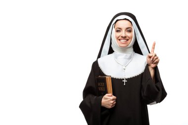 cheerful nun holding bible and pointing up with idea isolated on white clipart