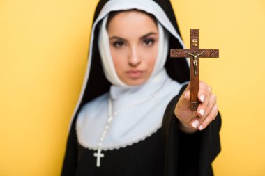 selective focus of beautiful nun holding cross isolated on yellow clipart