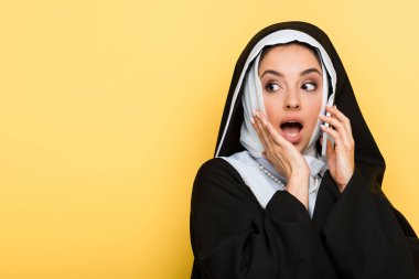 Güzel, şaşkın bir rahibe, sarı bir telefondan konuşuyor.