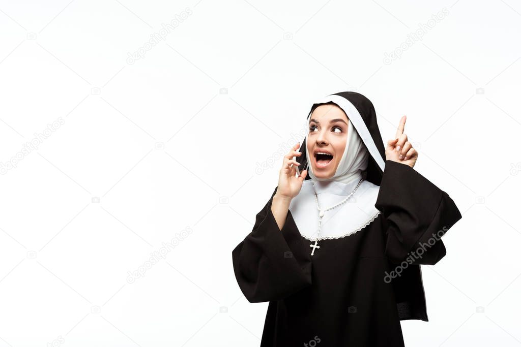 beautiful emotional nun talking on smartphone while pointing up isolated on white