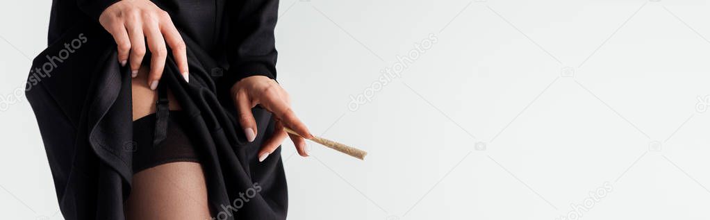 panoramic shot of sexy nun in stockings holding marijuana joint isolated on grey