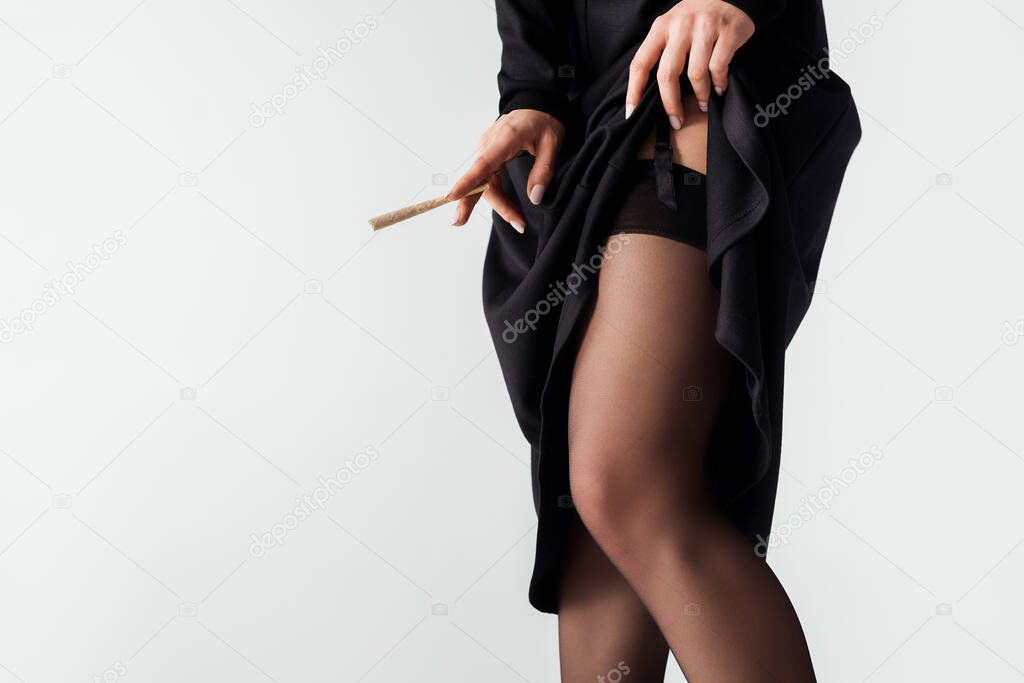 cropped view of seductive nun in stockings holding marijuana joint isolated on grey
