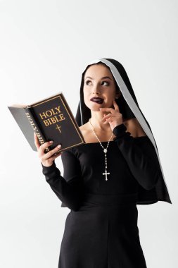 pensive sexy nun in black dress reading bible isolated on grey clipart