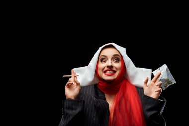 excited demoniac nun holding marijuana joint and buds isolated on black clipart