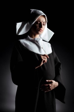 worried pregnant nun holding cross and touching belly on grey clipart
