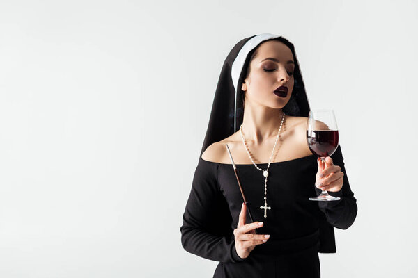 beautiful sensual nun holding glass of wine and cigarette in mouthpiece isolated on grey 