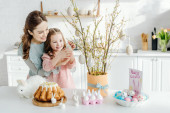 glückliches Kind berührt dekoratives Osterei auf Weidenzweig in der Nähe der Mutter 