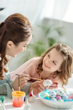 Mutlu anne ve neşeli kız Paskalya yumurtaları boyuyor. 