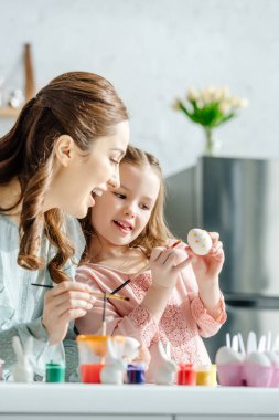 Süslü tavşanların yanında paskalya yumurtası boyayan çekici anne ve tatlı kızın seçici odağı. 