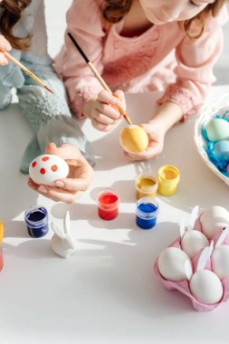 Anne ve çocuğun paskalya yumurtalarını dekoratif tavşanın yanında boyarken çekilmiş görüntüsü. 